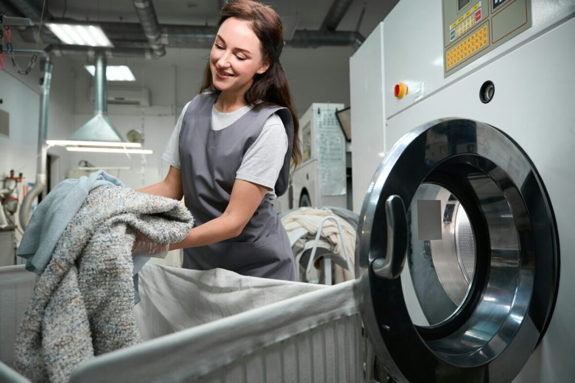 dry-cleaning-service-worker-loading-industrial-washing-machine-with-clothes